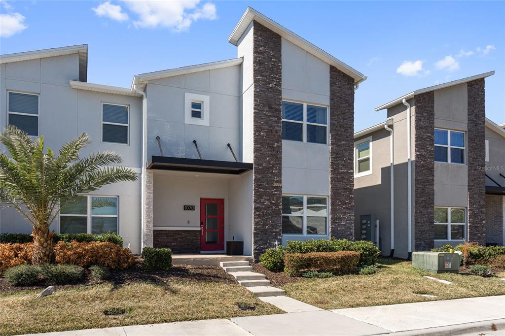 A modern two-story townhouse features a red front door, stone accents, and a palm tree — 1070 SPLASH SHOT PLACE, DAVENPORT, FL