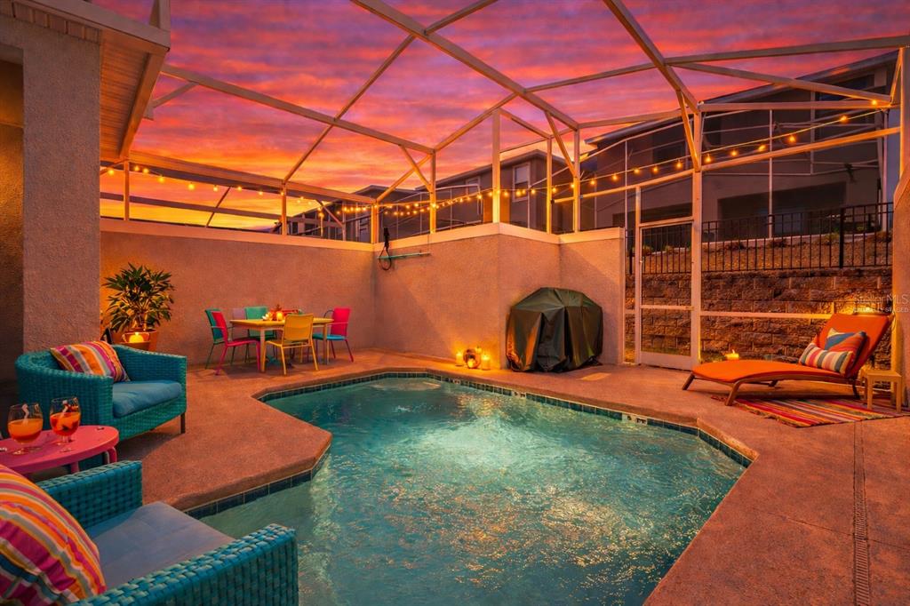 A screened-in patio features a swimming pool, outdoor furniture, and string lights at sunset — 1070 SPLASH SHOT PLACE, DAVENPORT, FL