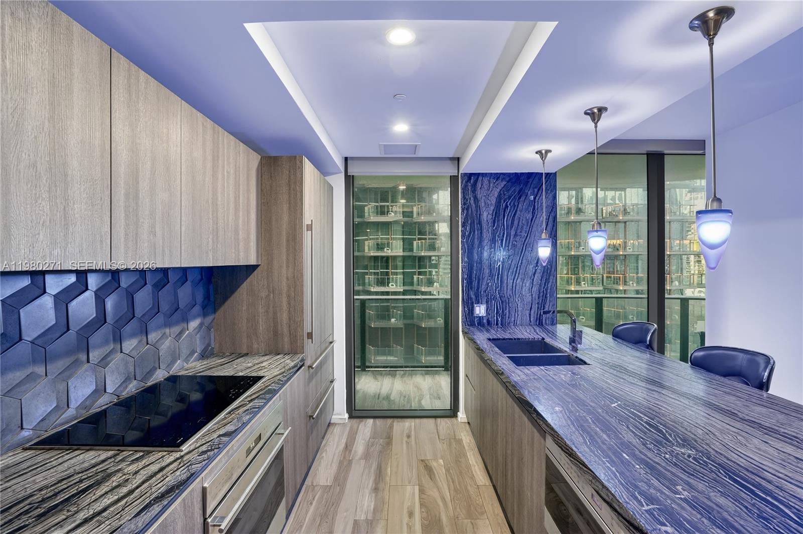 A modern kitchen features blue stone countertops, wood cabinetry, and a glass door to a balcony — 801 S Miami Ave # 2805, Miami FL 33130, MIAMI, FL
