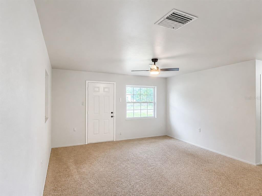 A carpeted room features a white door, a window, and a ceiling fan — 38401 FERGUSON AVE, DADE CITY, FL