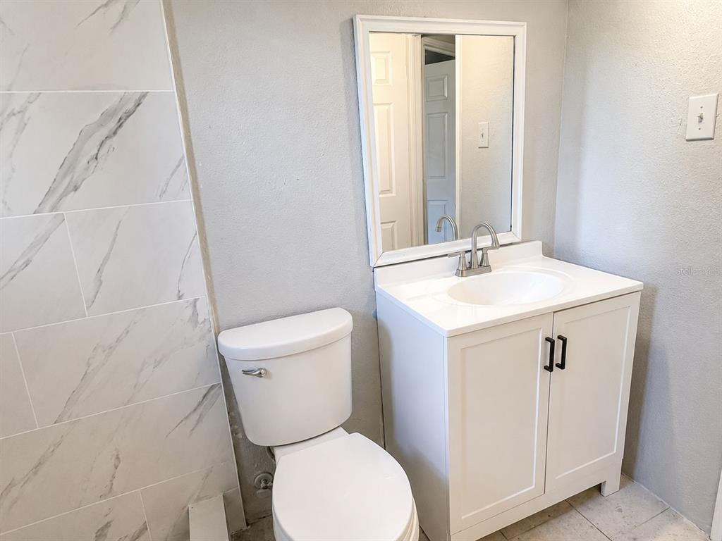 A bathroom features a white vanity, a toilet, and a marble-patterned tiled shower wall — 38401 FERGUSON AVE, DADE CITY, FL