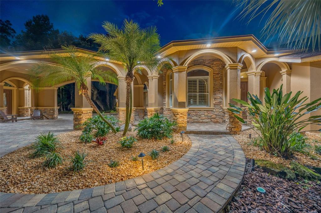 A stone-paved walkway leads to the arched, covered entrance of a stucco home at night — 7519 YARDLEY WAY, TAMPA, FL