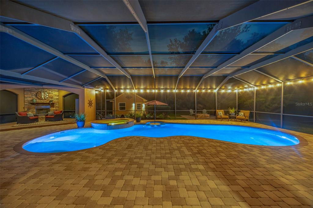 A screened-in patio features a freeform swimming pool, a hot tub, and stone pavers — 7519 YARDLEY WAY, TAMPA, FL