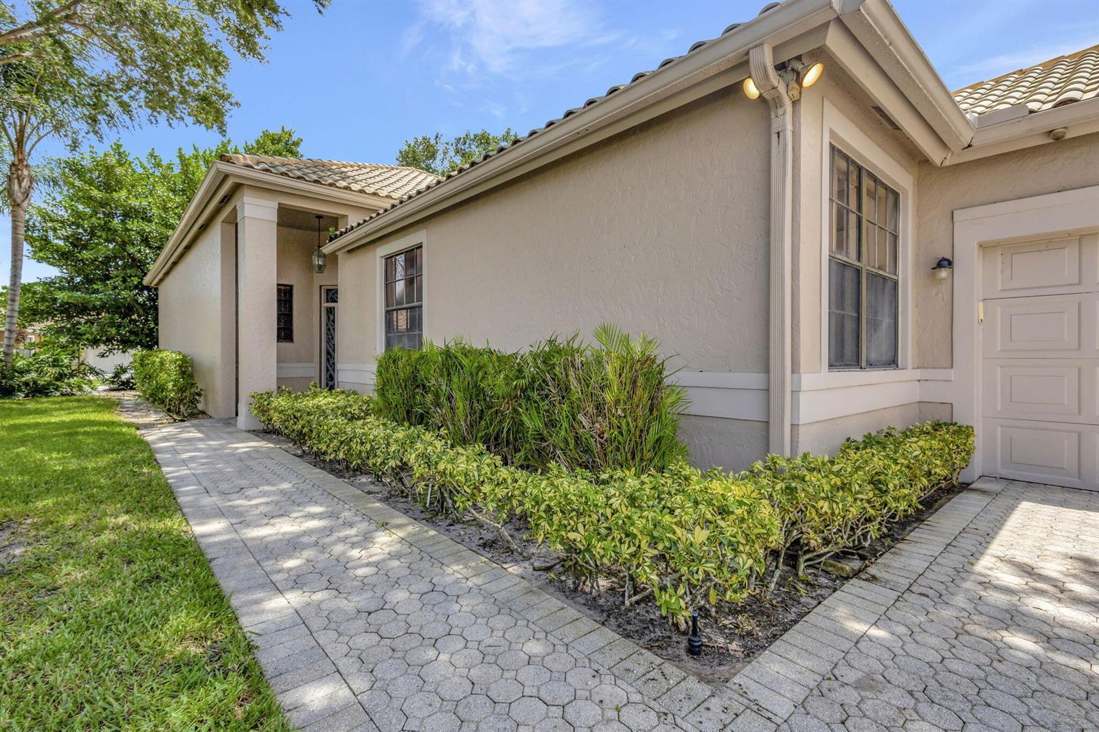 A paved walkway leads to the front entrance of a beige house with a garage — 4528 Barclay Fair Way, Lake Worth FL 33449, LAKE WORTH, FL