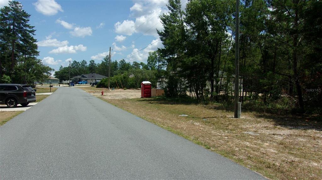 A paved road leads past a vacant lot with a portable toilet and trees — 0 SW 131ST PLACE ROAD, OCALA, FL