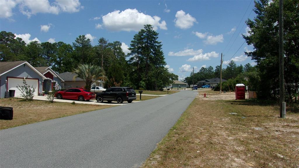 A paved residential street with houses, parked cars, and a portable toilet on the right — 0 SW 131ST PLACE ROAD, OCALA, FL