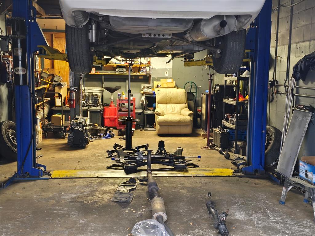 A car is elevated on a lift inside a cluttered automotive repair garage — 2719 OLD DIXIE HWY, KISSIMMEE, FL