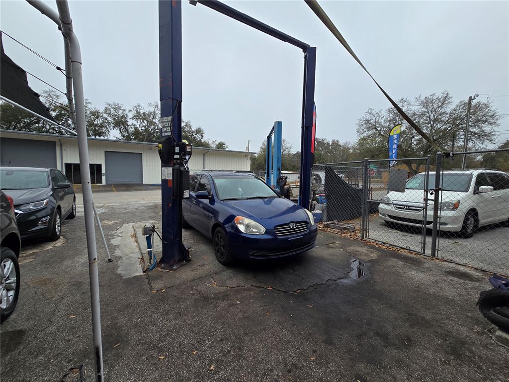 A blue sedan is parked under a vehicle lift in an outdoor automotive service area — 2719 OLD DIXIE HWY, KISSIMMEE, FL