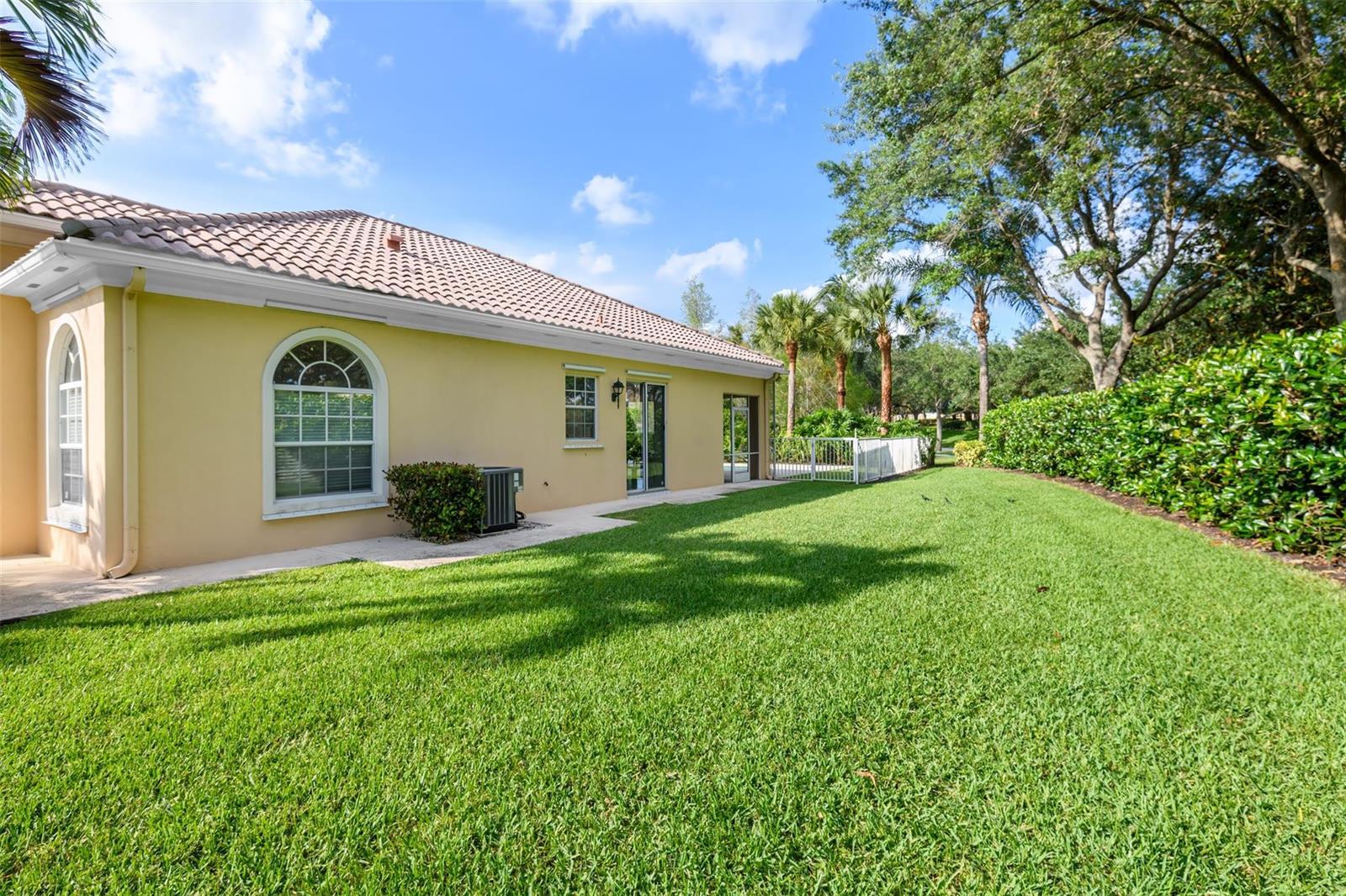 The exterior of a yellow house with a tiled roof overlooks a grassy backyard — 8019 Nevis Place, Wellington FL 33414, WELLINGTON, FL