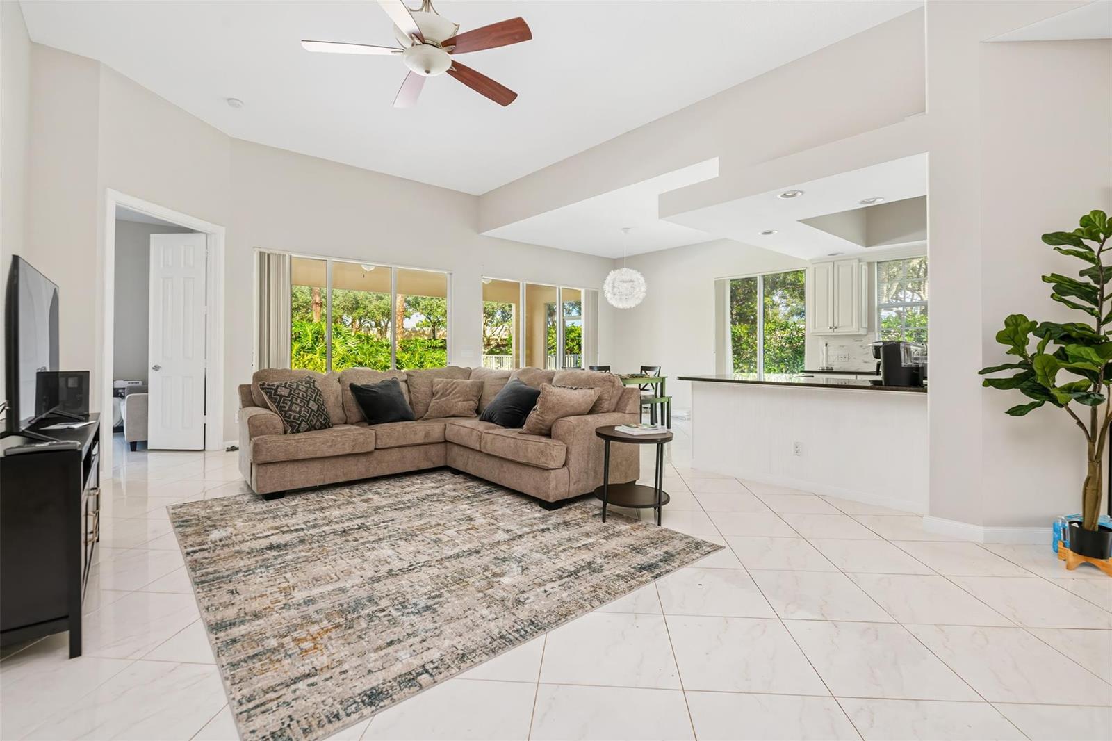 A living room with a sectional sofa, tile floors, and an open kitchen area — 8019 Nevis Place, Wellington FL 33414, WELLINGTON, FL