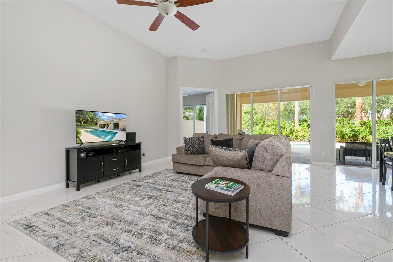 A living room features a sectional sofa, a television on a console, and sliding glass doors — 8019 Nevis Place, Wellington FL 33414, WELLINGTON, FL