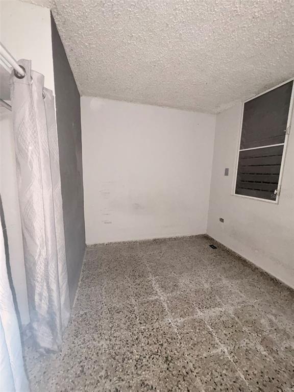 An empty room features speckled tile flooring, white walls, a textured ceiling, and a window — Calle Geminis 13, CANOVANAS, PR