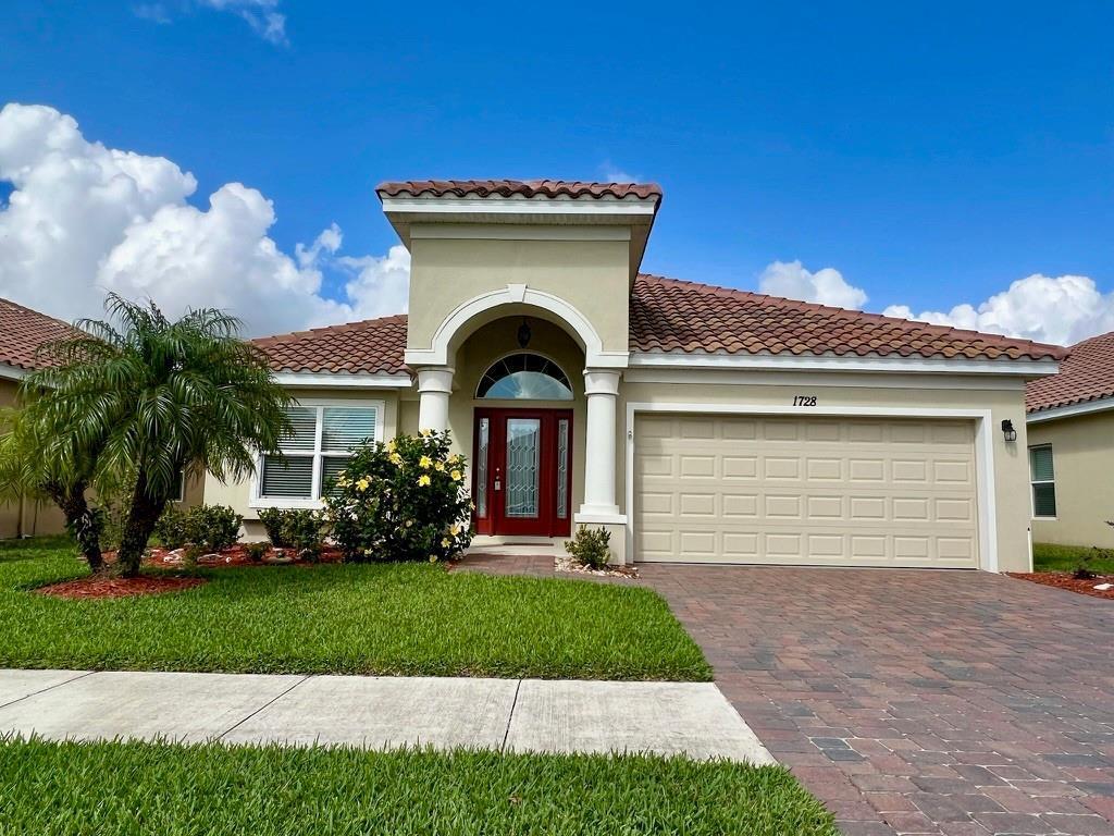 A single-story house with a red front door, arched entryway, and a paved driveway — 1728 Berkshire Circle SW, Vero Beach FL 32968, VERO BEACH, FL