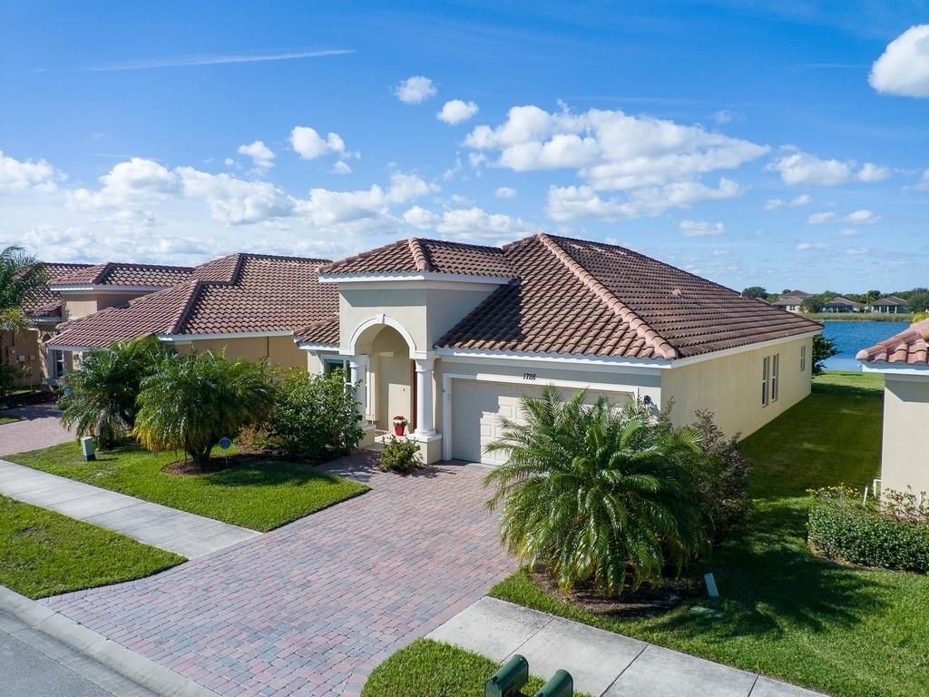 An aerial view shows a single-story house with a tiled roof, paver driveway, and palm trees — 1728 Berkshire Circle SW, Vero Beach FL 32968, VERO BEACH, FL