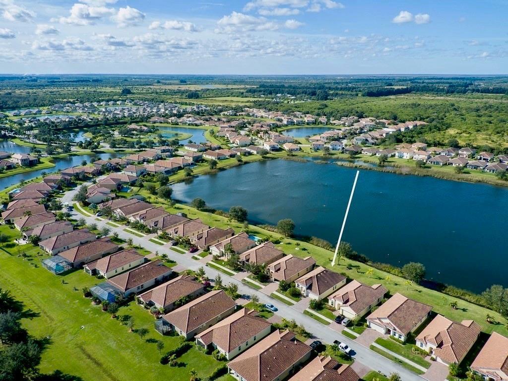 An aerial view shows a suburban neighborhood with houses bordering a large lake — 1728 Berkshire Circle SW, Vero Beach FL 32968, VERO BEACH, FL