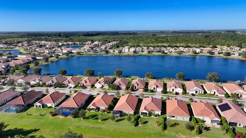 An aerial view shows a suburban neighborhood with houses surrounding a large central lake — 1728 Berkshire Circle SW, Vero Beach FL 32968, VERO BEACH, FL