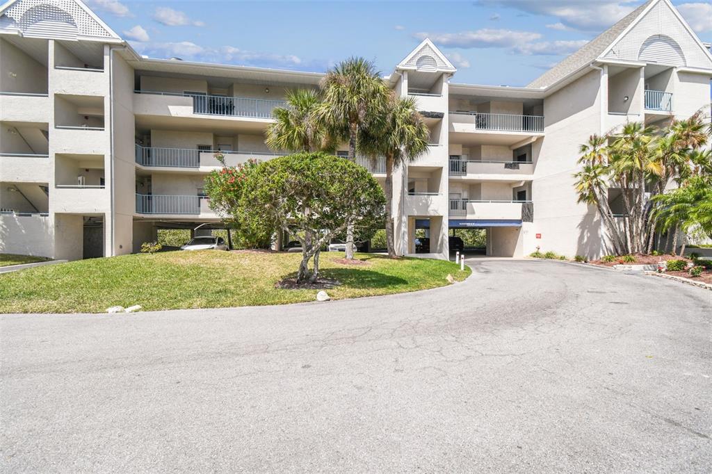 A multi-story apartment building features balconies, palm trees, and a ground-level parking area — 5537 SEA FOREST DRIVE UNIT 301, NEW PORT RICHEY, FL