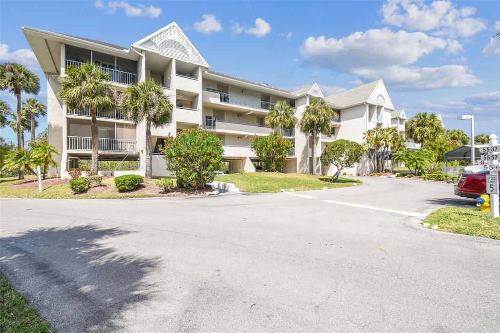 A multi-story apartment building with screened balconies and palm trees in a landscaped setting — 5537 SEA FOREST DRIVE UNIT 301, NEW PORT RICHEY, FL