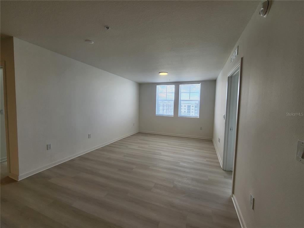 An empty room features light-colored wood-look flooring, white walls, and two windows — 5579 MILLENIA PARK BLVD UNIT 509, ORLANDO, FL