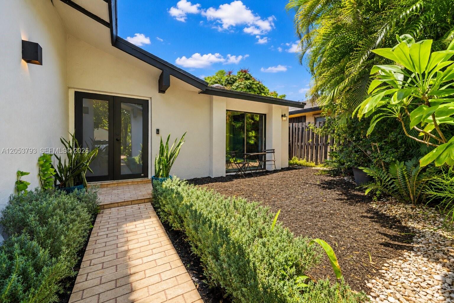 A brick walkway leads to a house exterior with a black-framed door and sliding glass doors — 10932 SW 135th Ct Cir, Miami FL 33186, MIAMI, FL