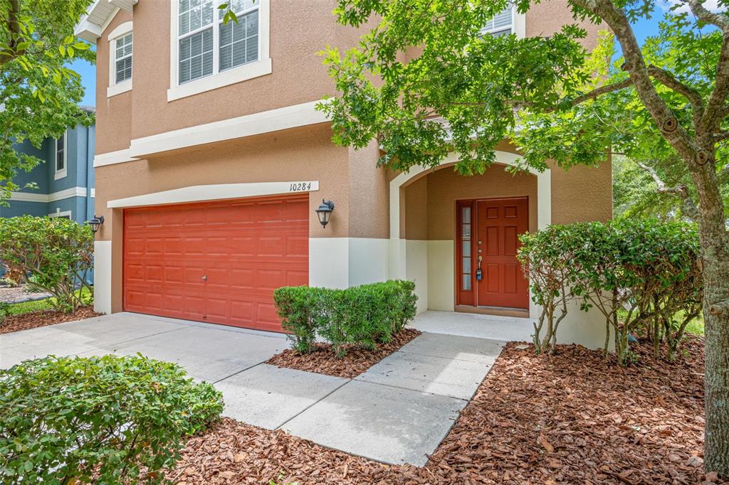 A two-story house exterior features a red garage door, matching front door, and concrete walkway — 10284 NEWMINSTER LOOP, RUSKIN, FL
