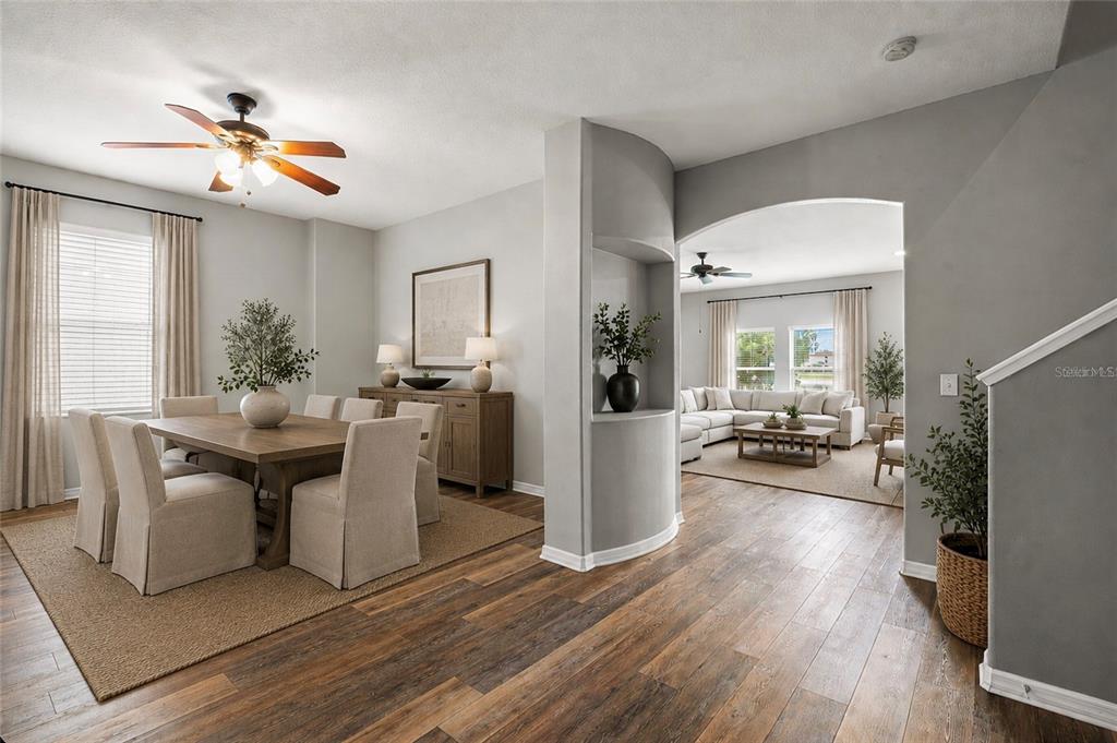 A dining room with a wooden table leads into a living room through an arched opening — 10284 NEWMINSTER LOOP, RUSKIN, FL