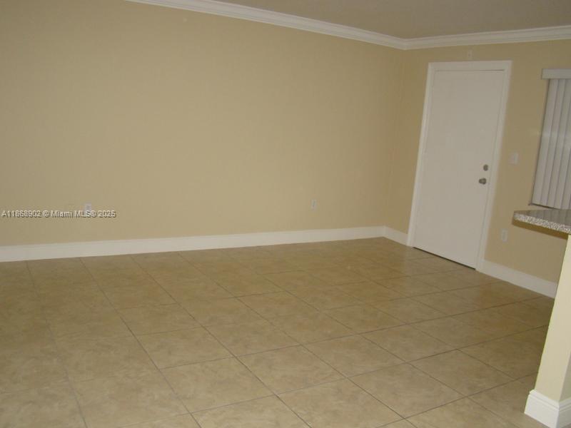 An empty room features beige walls, crown molding, and light-colored square floor tiles — 3901 SW 112th Ave # 46, Miami FL 33165, MIAMI, FL