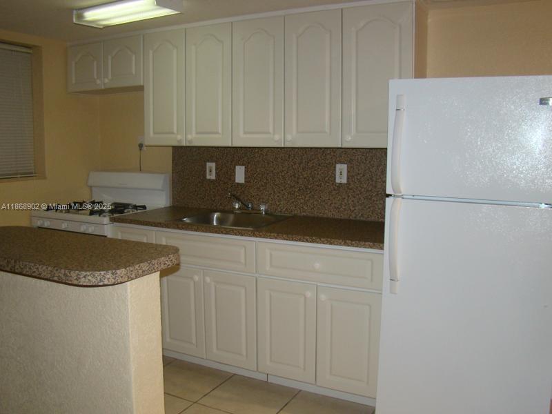 A kitchen features off-white cabinets, a speckled countertop, a white refrigerator, and a small peninsula — 3901 SW 112th Ave # 46, Miami FL 33165, MIAMI, FL
