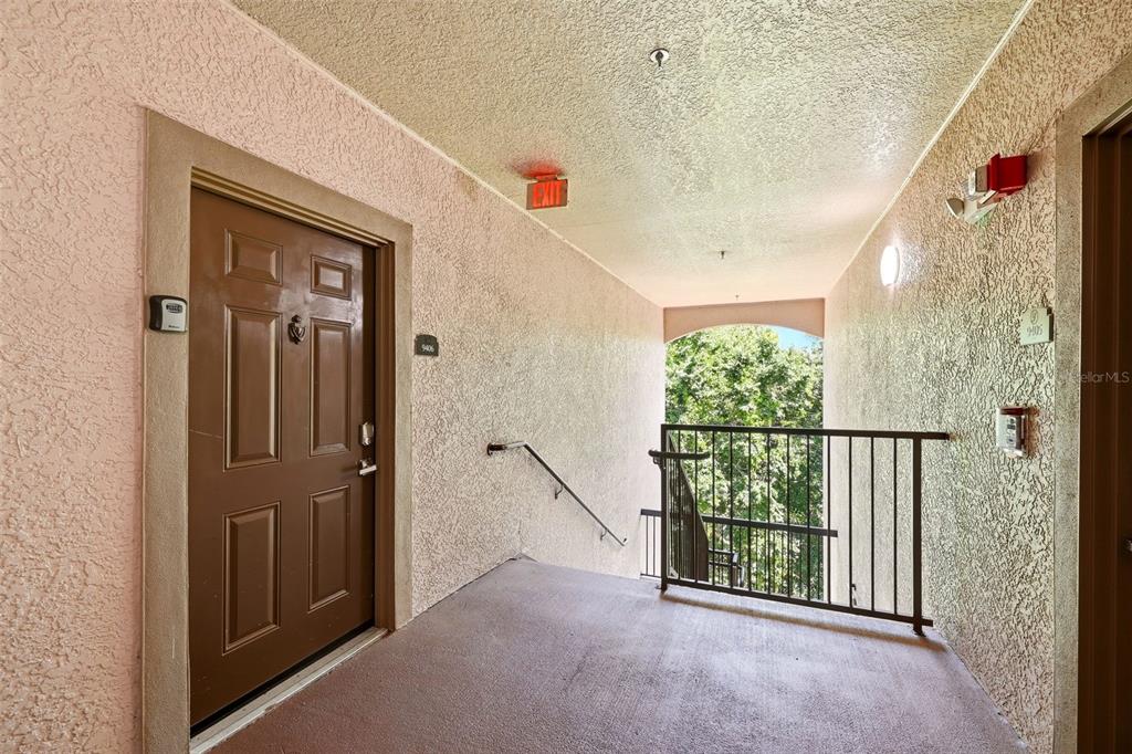 An outdoor apartment hallway features a brown door, a metal railing, and a staircase — 1301 TUSCAN TERRACE UNIT 9406, DAVENPORT, FL