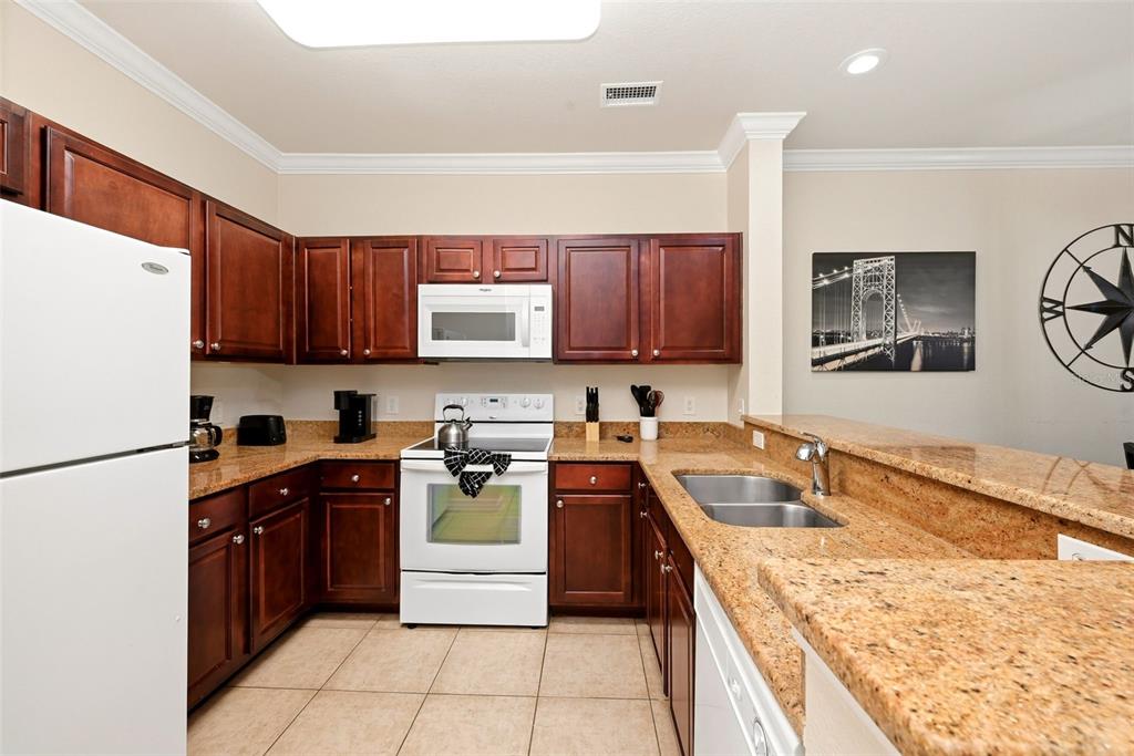 A kitchen features dark wood cabinets, granite countertops, white appliances, and tile flooring — 1301 TUSCAN TERRACE UNIT 9406, DAVENPORT, FL