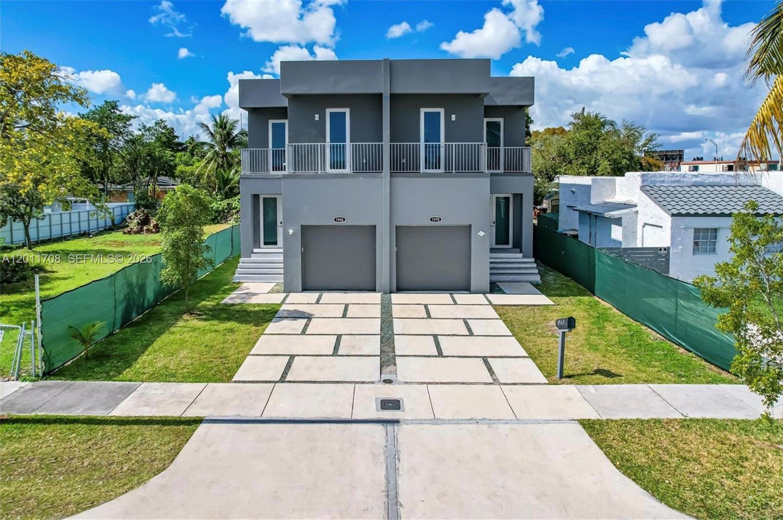 A modern two-story duplex features gray stucco siding, two garage doors, and a concrete driveway — 1968 NW 25th Ave # 1968, Miami FL 33125, MIAMI, FL