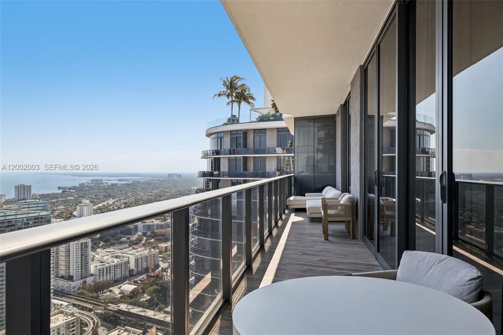 A high-rise balcony features a glass railing, outdoor seating, and panoramic city and water views — 801 S Miami Ave # 4902, Miami FL 33130, MIAMI, FL