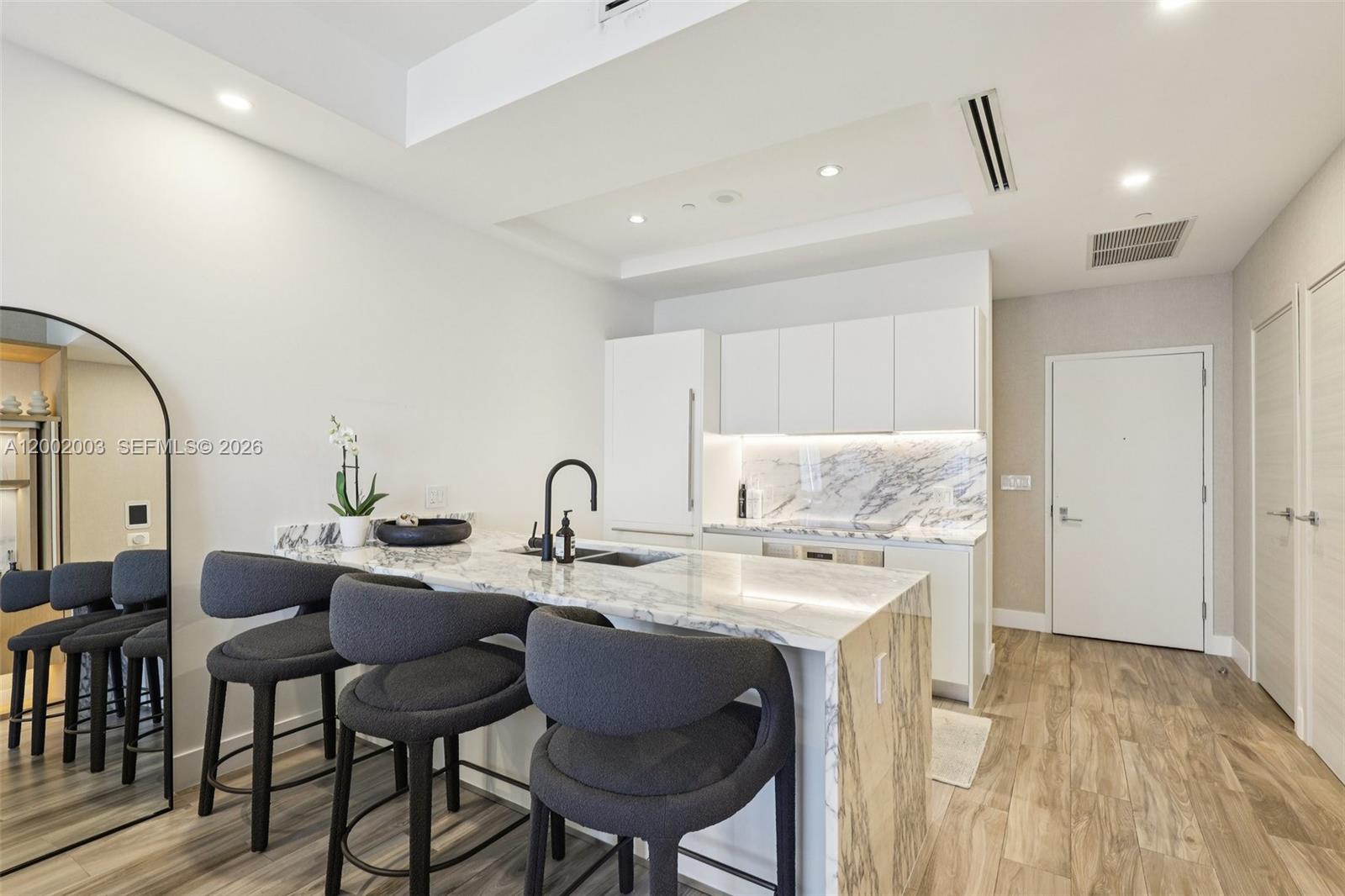 A modern kitchen features a marble waterfall island, dark bar stools, and white cabinetry — 801 S Miami Ave # 4902, Miami FL 33130, MIAMI, FL