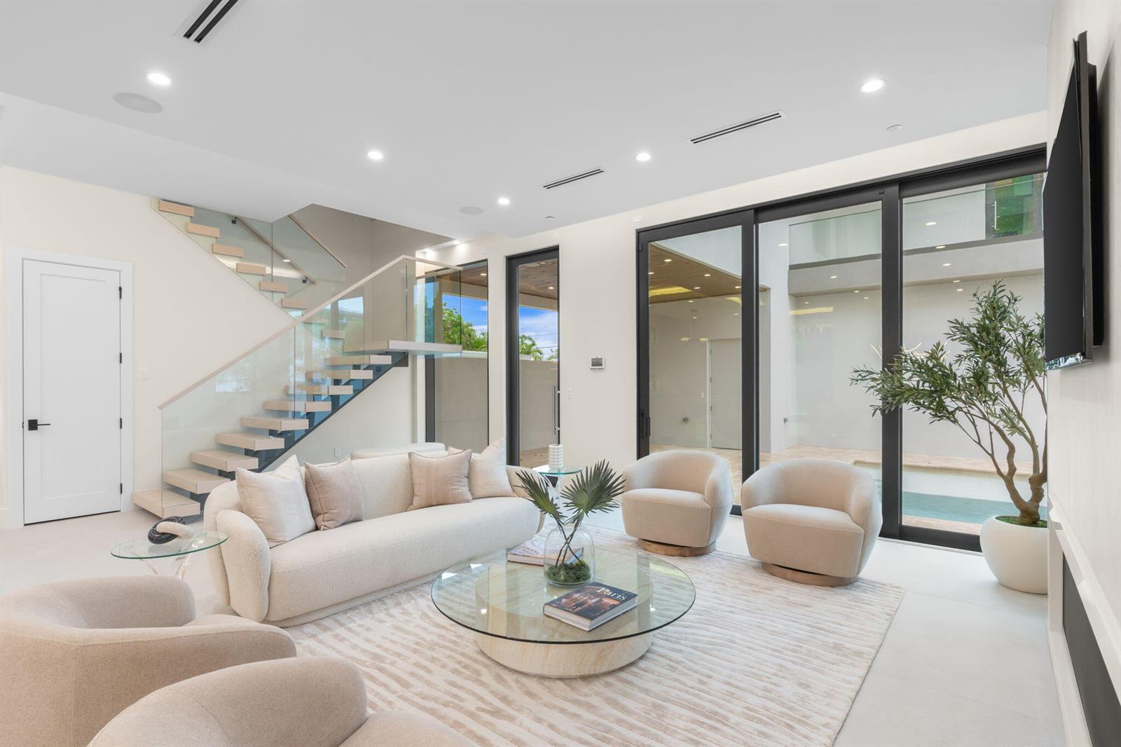 A modern living room features a glass-railed staircase, neutral furniture, and large sliding glass doors — 301 NE 7th Avenue, Delray Beach FL 33483, DELRAY BEACH, FL