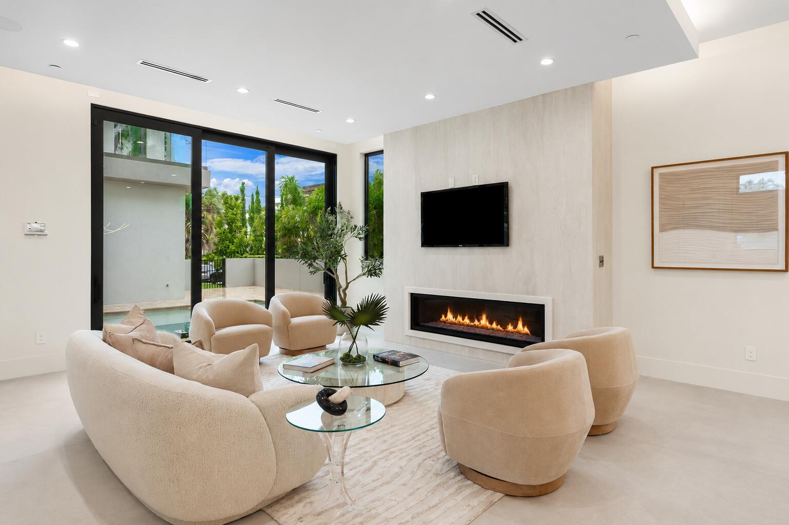 A modern living room features a fireplace, wall-mounted television, curved furniture, and floor-to-ceiling glass doors — 301 NE 7th Avenue, Delray Beach FL 33483, DELRAY BEACH, FL