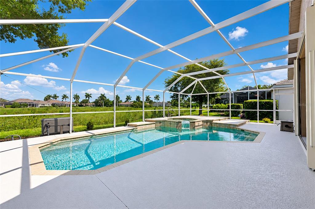 A screened-in swimming pool and spa overlook a grassy field under a blue sky — 5133 FLAGSTONE DRIVE, SARASOTA, FL