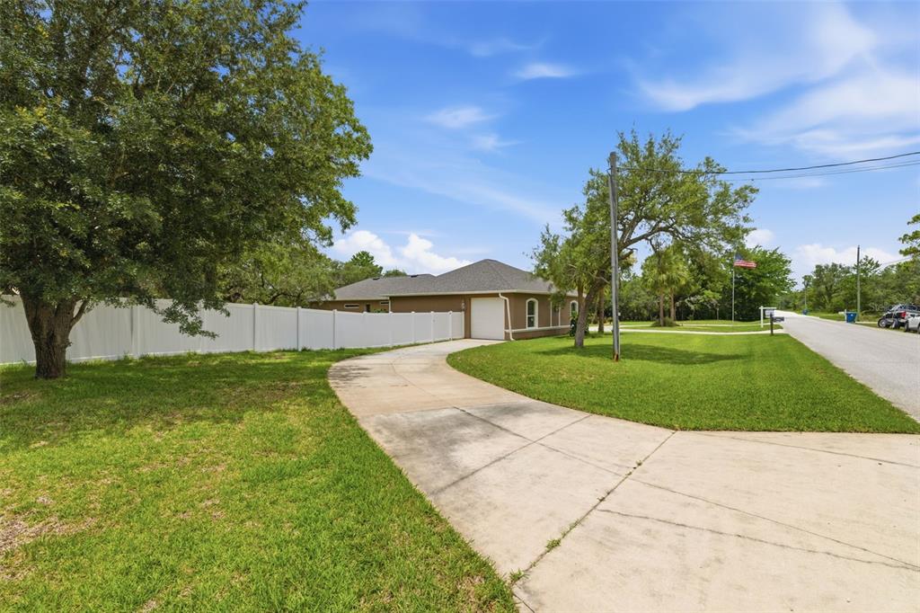 A concrete driveway leads to the side-entry garage of a house with a white fence — 11145 MOUNTAIN MOCKINGBIRD RD, WEEKI WACHEE, FL
