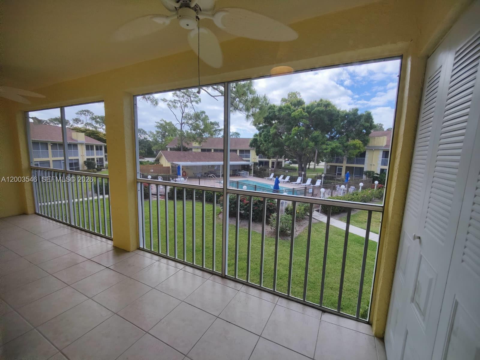 A screened-in balcony with tile flooring overlooks a swimming pool and apartment buildings — 2668 Kings Lake # 2668, Naples FL 34112, NAPLES, FL