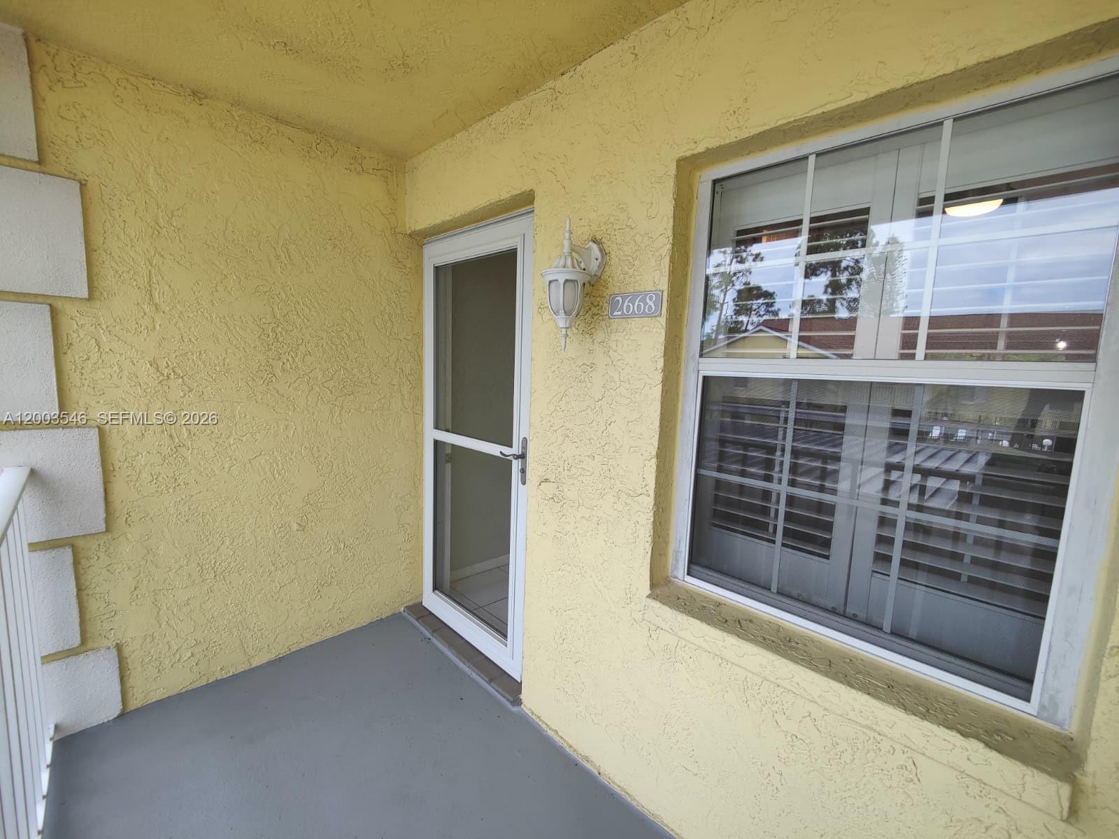 A yellow stucco exterior wall features a white screen door and a single window — 2668 Kings Lake # 2668, Naples FL 34112, NAPLES, FL