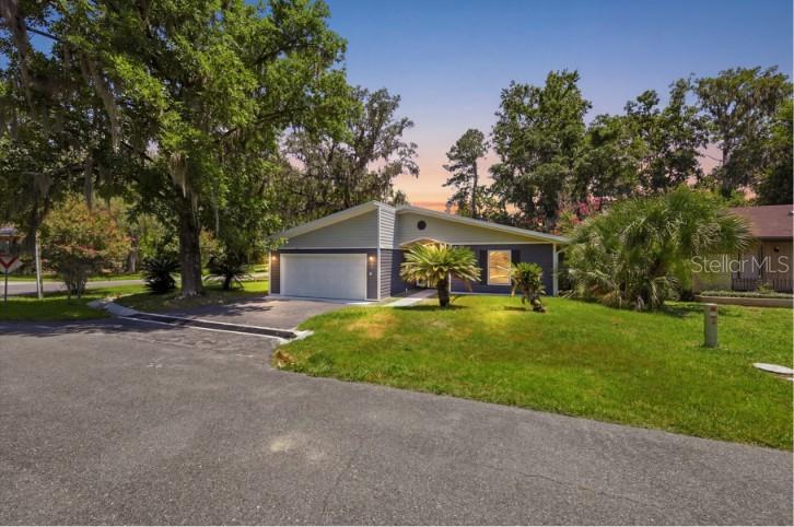 A single-story house with a two-car garage and a lawn sits under large trees — 6840 NW 111TH LANE, ALACHUA, FL