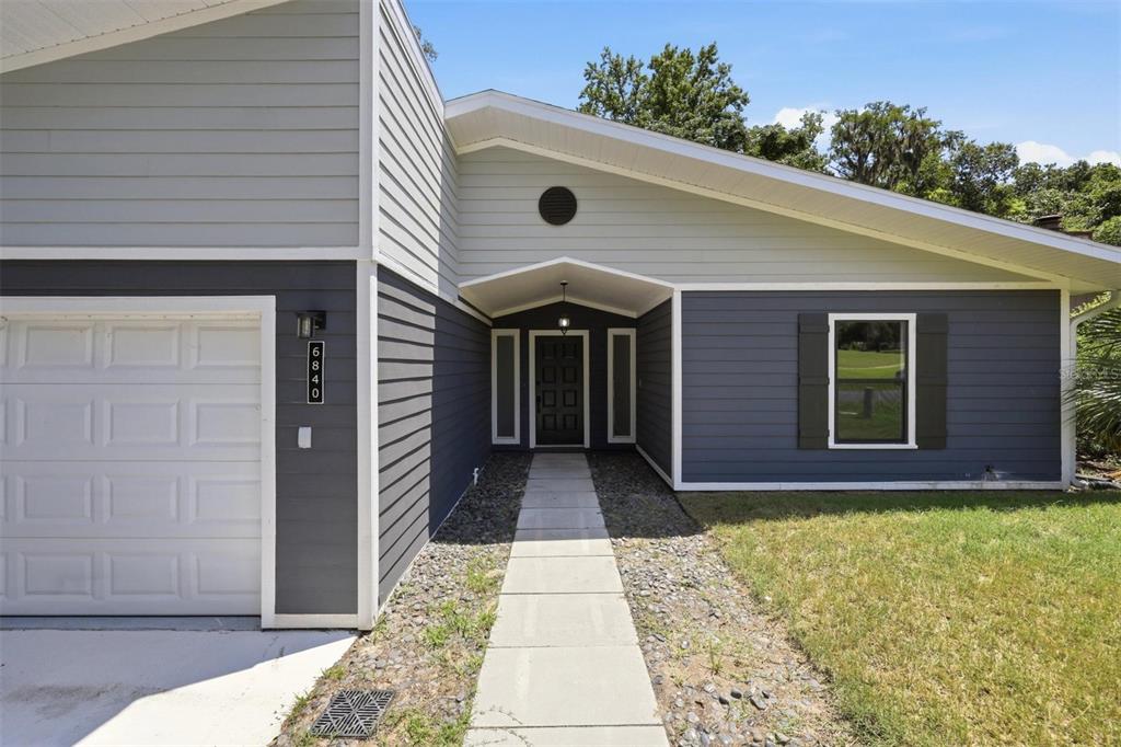A single-story house exterior features gray horizontal siding, a white garage door, and a walkway — 6840 NW 111TH LANE, ALACHUA, FL