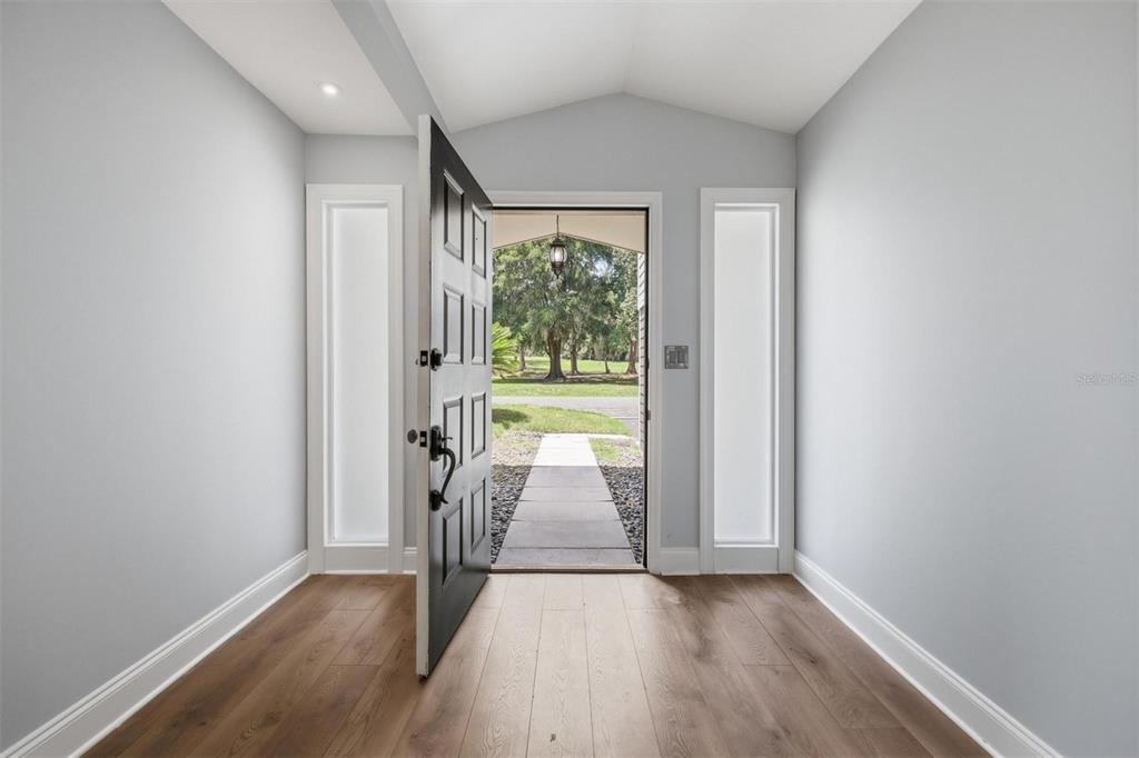 An entryway with light wood flooring, gray walls, and an open door revealing a walkway — 6840 NW 111TH LANE, ALACHUA, FL