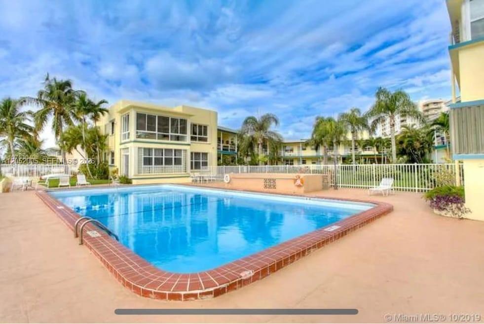 A swimming pool sits in front of a multi-story apartment building with palm trees — 910 Bay Dr # 9, Miami Beach FL 33141, MIAMI BEACH, FL