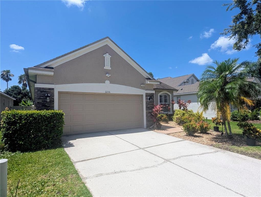 A beige house with a two-car garage and a concrete driveway under a blue sky — 11236 BLACKSMITH DRIVE, TAMPA, FL