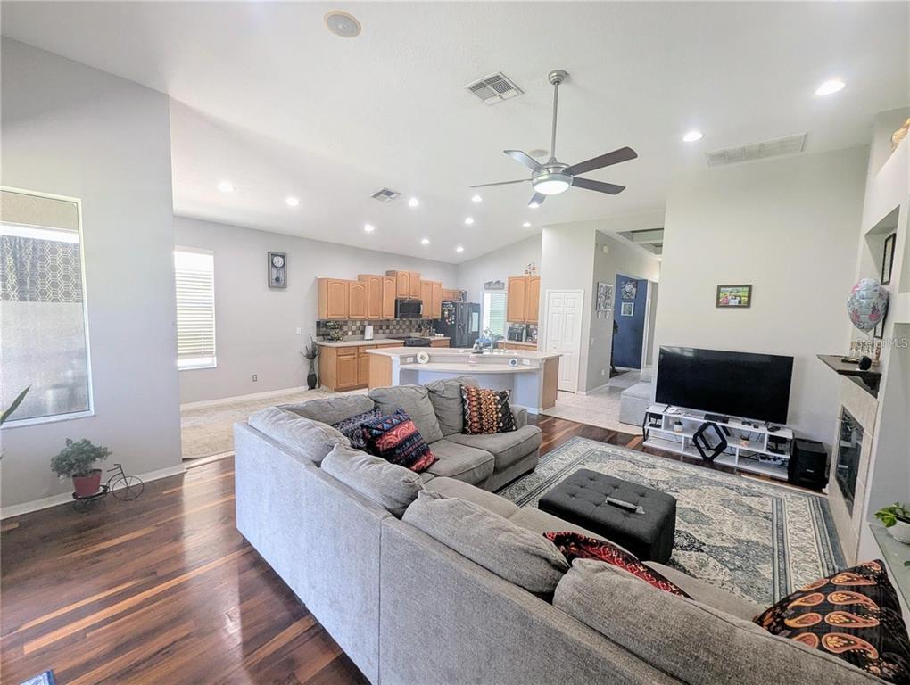 A spacious open-concept living room features a large sectional sofa, hardwood floors, and a kitchen — 11236 BLACKSMITH DRIVE, TAMPA, FL