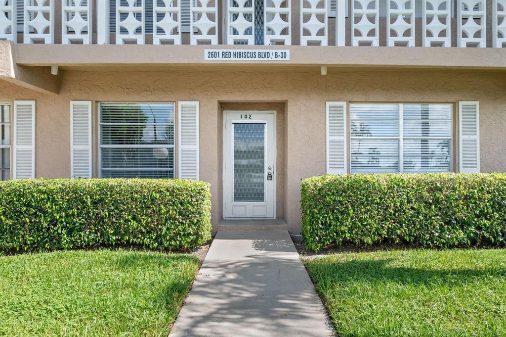 A ground-level apartment entrance features a white door, windows with shutters, and manicured hedges — 2601 Red Hibiscus Boulevard, Delray Beach FL 33445, DELRAY BEACH, FL