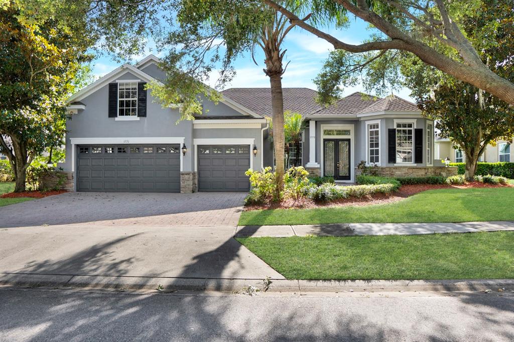 A gray single-story house with a three-car garage, brick driveway, and a landscaped front yard — 1771 LEE JANZEN DRIVE, KISSIMMEE, FL