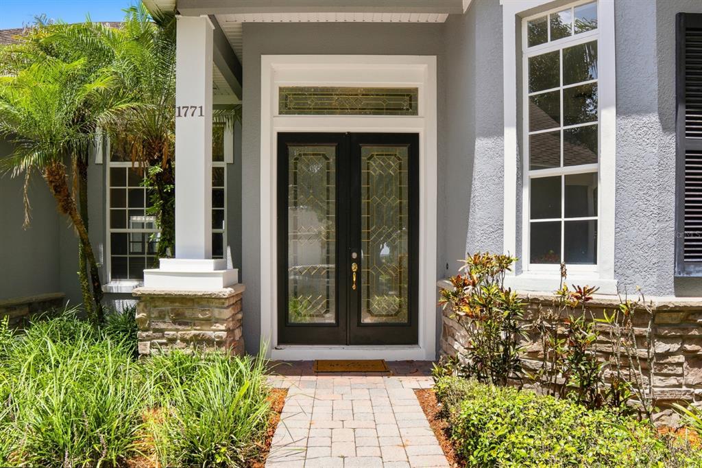 A paved walkway leads to the double front doors of a grey house with stone accents — 1771 LEE JANZEN DRIVE, KISSIMMEE, FL