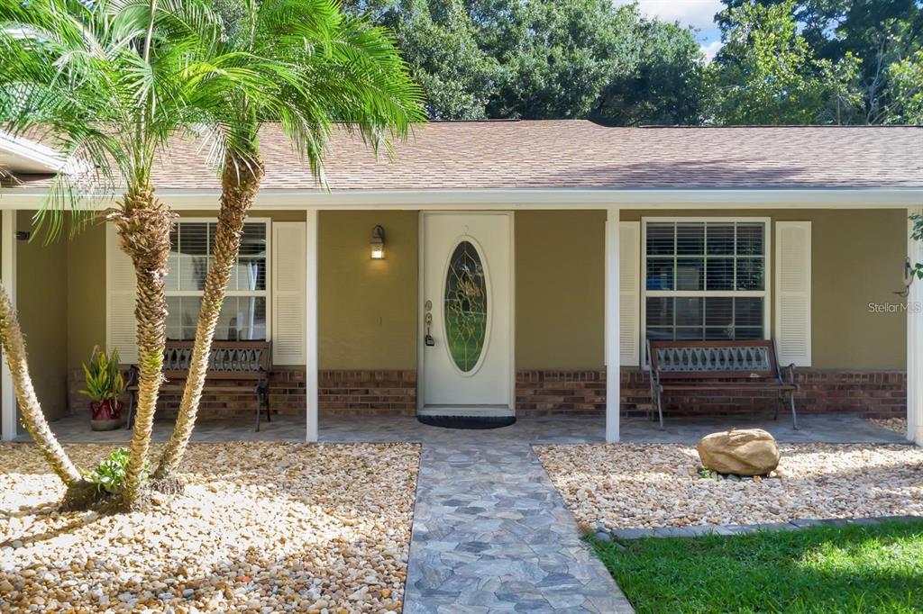 A single-story house exterior features a stone walkway, a palm tree, and two wooden benches — 2619 W PONKAN ROAD, APOPKA, FL
