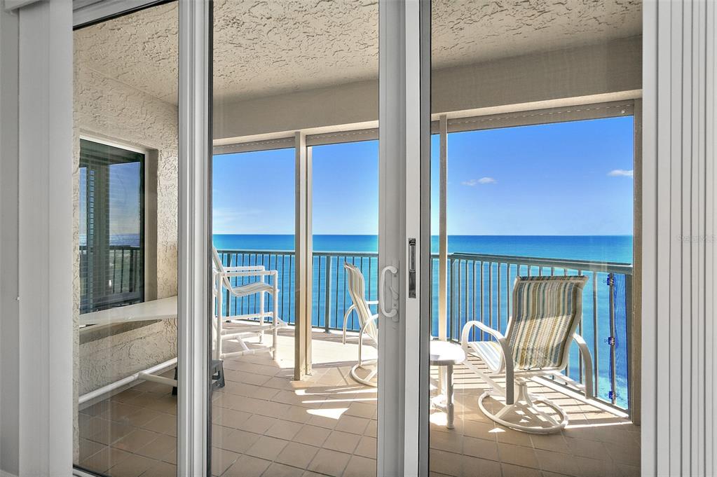 A view through sliding glass doors onto a balcony overlooking the ocean with patio furniture — 3425 S ATLANTIC AVENUE UNIT 1206, DAYTONA BEACH SHORES, FL
